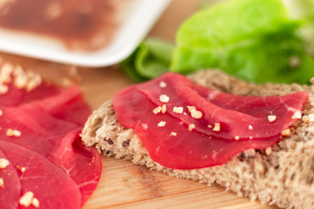 A slice of meat is on a wooden cutting board next to a plate. The meat is red and has a sprinkle of salt on itの写真素材