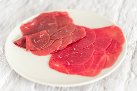 A plate of red meat with a white background. The meat is sliced into small pieces and arranged on the plateの写真素材