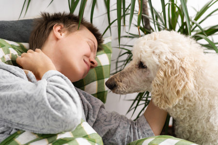 Engrossed in leisure, a middle-aged woman with short hair spends her time in bed with her big poodle. Laziness, weekend relaxationの写真素材