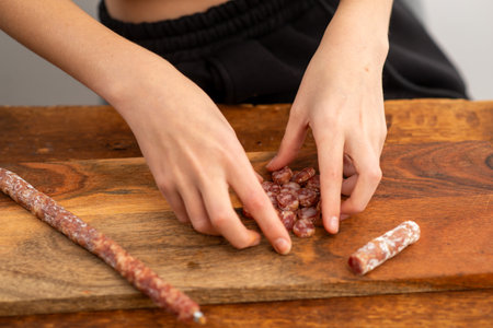 A person is cutting meat on a wooden cutting board. The meat is sausage and the person is using a...
