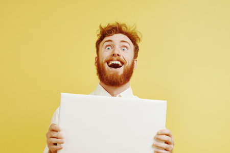 Happy Redhead Man Holding Blank Canvas Against Yellow Background.の素材