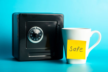 Black safe and white mug with 'safe' note against blue background.の写真素材