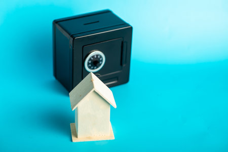 Secure savings: small wooden house and mini safe on blue background.の写真素材