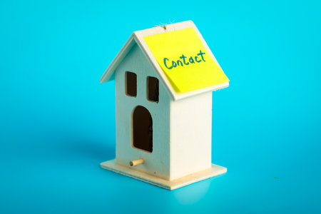 Wooden house piggy bank with sticky note label on blue background.の写真素材