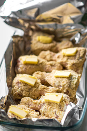 Golden baked chicken drumsticks with butter and breadcrumbs in foil tray.の写真素材