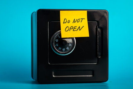 Secure black safe with combination lock and caution note over a vibrant blue background.の写真素材