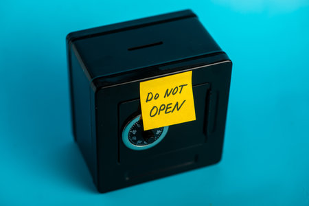 Secure black safe with "do not open" sticky note against bright blue background.の写真素材