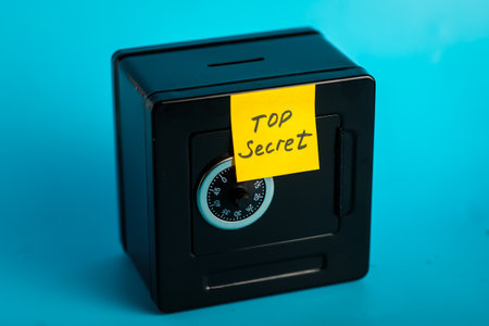 Small black safe with combination lock and "top secret" note on blue background.の写真素材