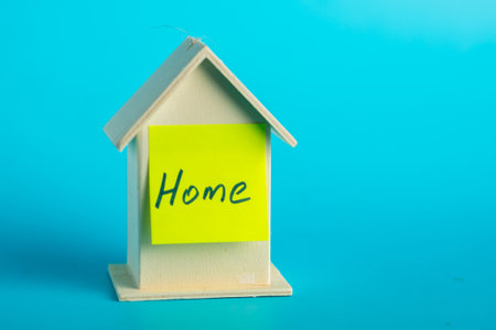 Wooden house model with yellow home note on blue background.の写真素材