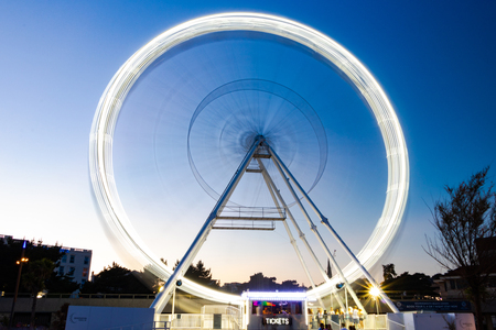 Bournemouth, United Kingdom- July 14, 2018: People are waiting to get on to the seasonal large Ferris wheel. Also known as Bournemouth Observation wheel. Long exposure shot, with blurred  people.のeditorial素材