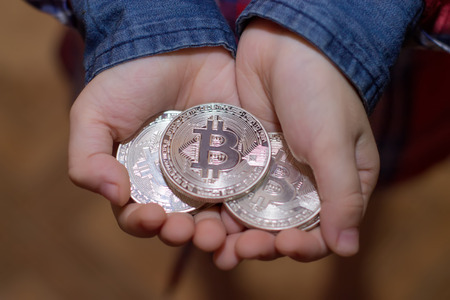 Bitcoin in the hands of a child. The boy holds a metal coin of crypto currency in his hands.の写真素材