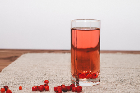 Glass with cranberry juice. Near the glass are a few cranberries. On a sackcloth and a wooden table.の写真素材