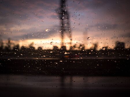 Blurred silhouette of industrial setting through car glass with raindrops against window. Sunset and...