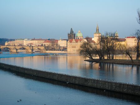 Cityscape of Prague with cathedral and charles bridge from other side of Vltave river. Reflections in water, copyspace available. Daylight with sun.の写真素材
