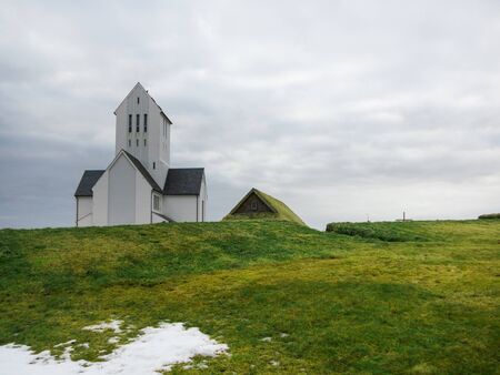 Skalholt church and ancient grass house on golden circle near Reykjavik, Iceland. Cloudy winter day with green hills and snow. No people.の写真素材