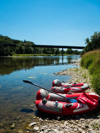 Two rafting boats with paddles laying on shore of beautiful natural river. Sunny summer day in Canada. Blue sky reflecting in water, no people visible.の写真素材