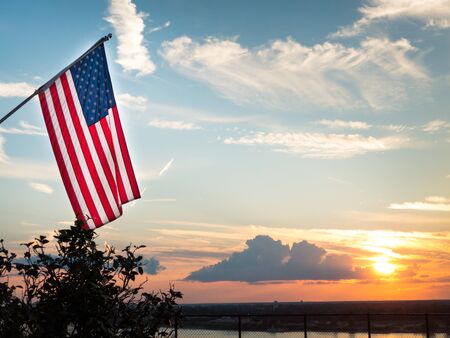Bright american flag flying high above beautiful sunset over Mississippi river. Symbol for patriotism and peace. Background shows illuminated clouds in the sky, copyspace, no peopleの写真素材