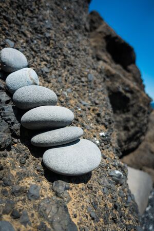 Close-up of zen-like stack of pebble stones leaning against black lava rocks on icelandic coast. Sunny daylight shot, no people visible.の写真素材