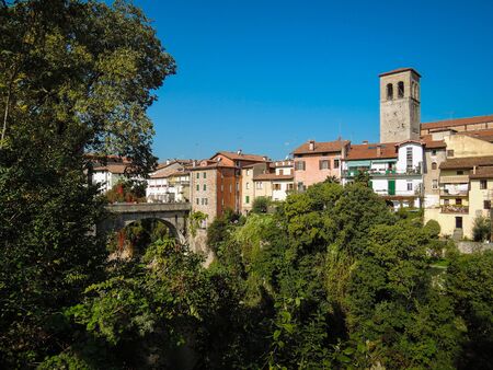 Beautiful landscape shot of Cividale del Friuli with trees in front of historic village and belltower. Medieval townscape with blue summer sky. No people.の写真素材