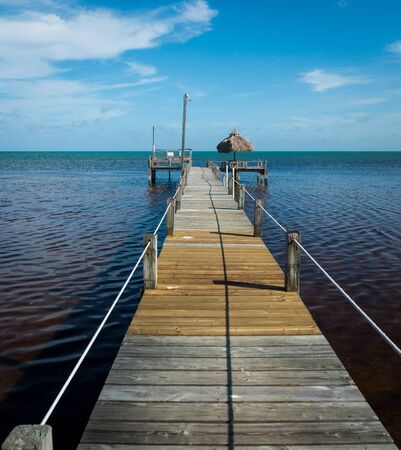 Wooden pier with tiki hut leading into the gulf of Mexico near Marathon on Florida keys. Blue sky with few clouds, sunny day. Vacation or travel shot, no people. copyspace.の写真素材