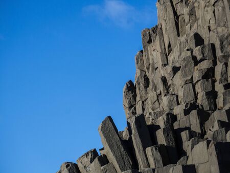 Beautiful natural basalt rock formation near Vik, Iceland at Reynisfjara beach. Column-shaped black lava rocks rising up into clear blue sky. Sunny, late afternoon. No people visible.の写真素材
