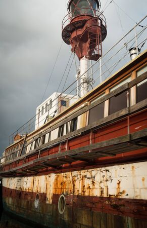 Old and partial rusty red and white houseboat on Copenhagen canal with cloudy grey sky. No people visible.の写真素材