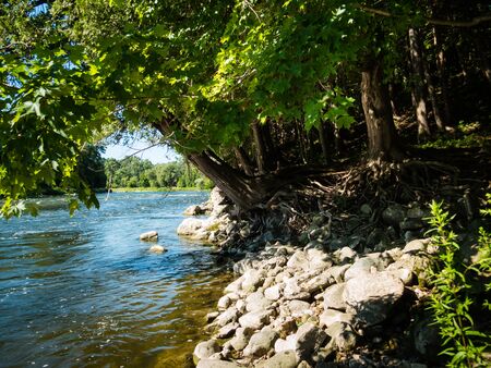 Beautiful natural river with trees and rocky river bank near Toronto, Ontario, Canada. Tranquil and calm setting. Sunny day, daylight. No people visible.の写真素材