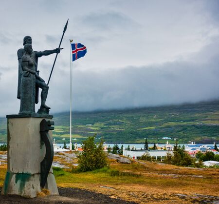 Landnemar status in Akureyri Iceland pointing to icelandic flag on cloudy day. Mountains and fog in background, Great abstract. No people visible.の写真素材
