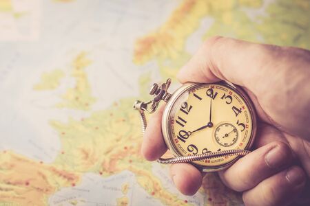 Holding old pocket watch in hand with map of Europe behind