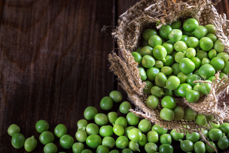 Green peas in small burlap bag on dark wooden background. Top view with copy spaceの写真素材