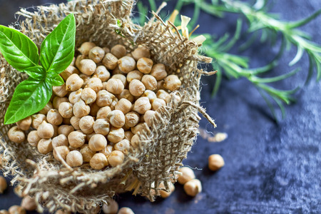 Garbanzo beans (chickpeas) with basil in small burlap bag on black rustic background. Top view with copy spaceの写真素材