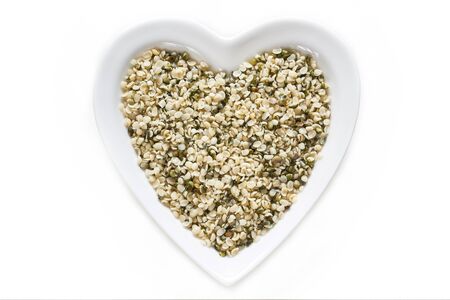Hemp seeds in heart shaped ceramic bowl isolated on white background. Top viewの写真素材