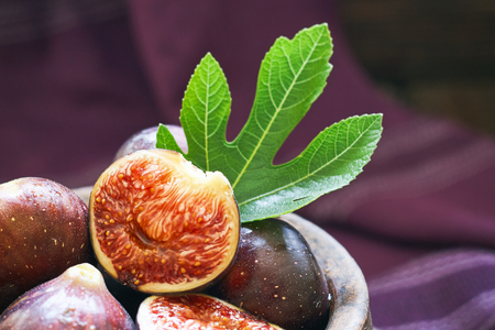 Fresh ripe black figs and fig leaf in rustic bowl on purple background. Copy spaceの写真素材