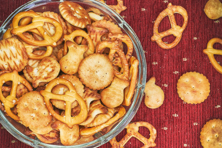 Mix of salty snacks (crackers and pretzels) in glass bowl on red backgroundの写真素材