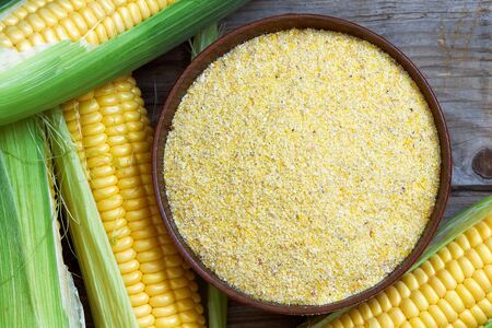 Organic maize flour in wooden bowl with fresh corn. Top view