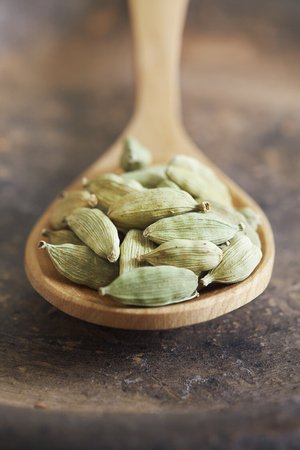 Raw green cardamom pods in wooden spoon on rustic backgroundの写真素材