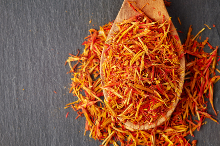 Safflower petals (Saffron substitute) in wooden spoon on black background. Top view with copy spaceの写真素材