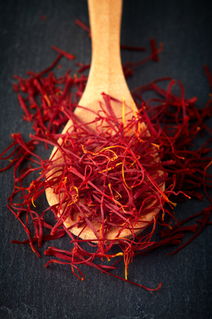 Saffron spice threads (strands) in wooden spoon on black backgroundの写真素材