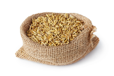 Oat seeds (Avena sativa) also known as the common oat in burlap sack isolated on white backgroundの写真素材