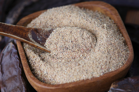 Ground carob (Ceratonia siliqua) powder in wooden bowlの写真素材