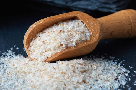 Psyllium (ispaghula) husk in wooden scoop on black rustic background