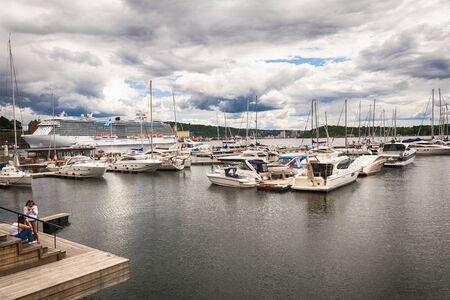Oslo, Norway - July 18, 2016: People enjoying the summer sunshine beside the al fresco restaurants and modern apartment buildings of Aker Brygge, the popular leisure district on the Oslo waterfront overlooking the marinas of Oslofjrden, Norway.のeditorial素材
