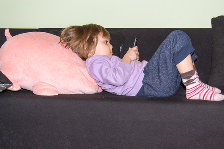 Cute little girl lying on the bed with her stuffed toy pig and mobile phoneの写真素材