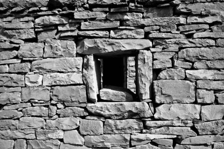 Very old and broken brick wall with a window in it 