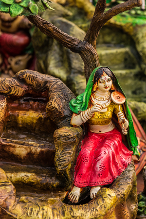 Miniature clay model of a village girl playing musical instrument beside a fountain.の写真素材