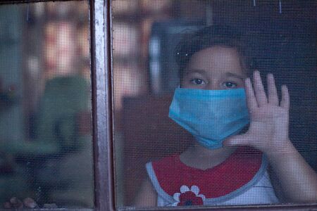 Little child looking outside from the door of home with mask on face with a hope of ending Pandemic Corona virusの写真素材