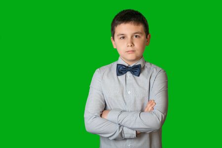 A serious child with a tie stands before the green backgroundの写真素材
