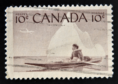 CANADA - CIRCA 1955: stamp printed in Canada shows Eskimo on a kayak against the background an iceberg, circa 1955 のeditorial素材