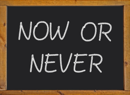 Now or never written on a blackboardの写真素材