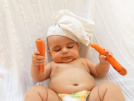 4 months old baby boy , baby chef, baby cook playing with carrots, white backgroundの写真素材